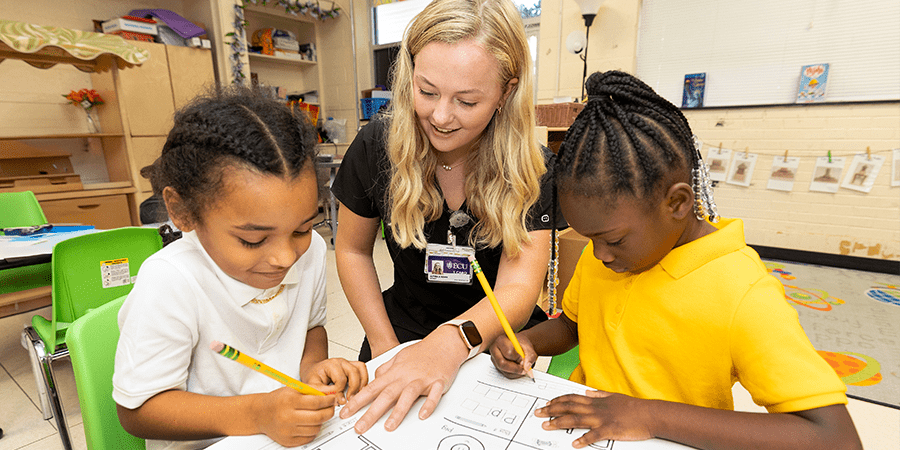 Young female teacher helping two elementary students with schoolwork