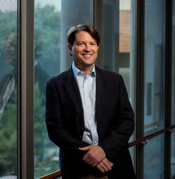 Dr. Jeffrey Stringer, smiling and leaning against a wall of windows.