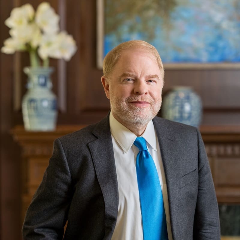 Peter Hans standing in front of a wooden fireplace mantel adorned with blue and white vases and white flowers.